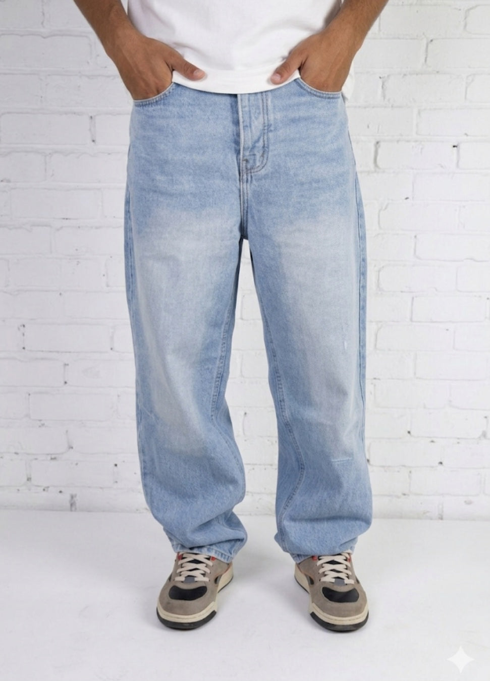 Person wearing light blue jeans and a white shirt against a white brick wall.