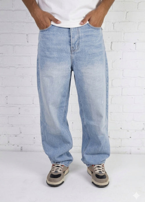 Person wearing light blue jeans and a white shirt against a white brick wall.